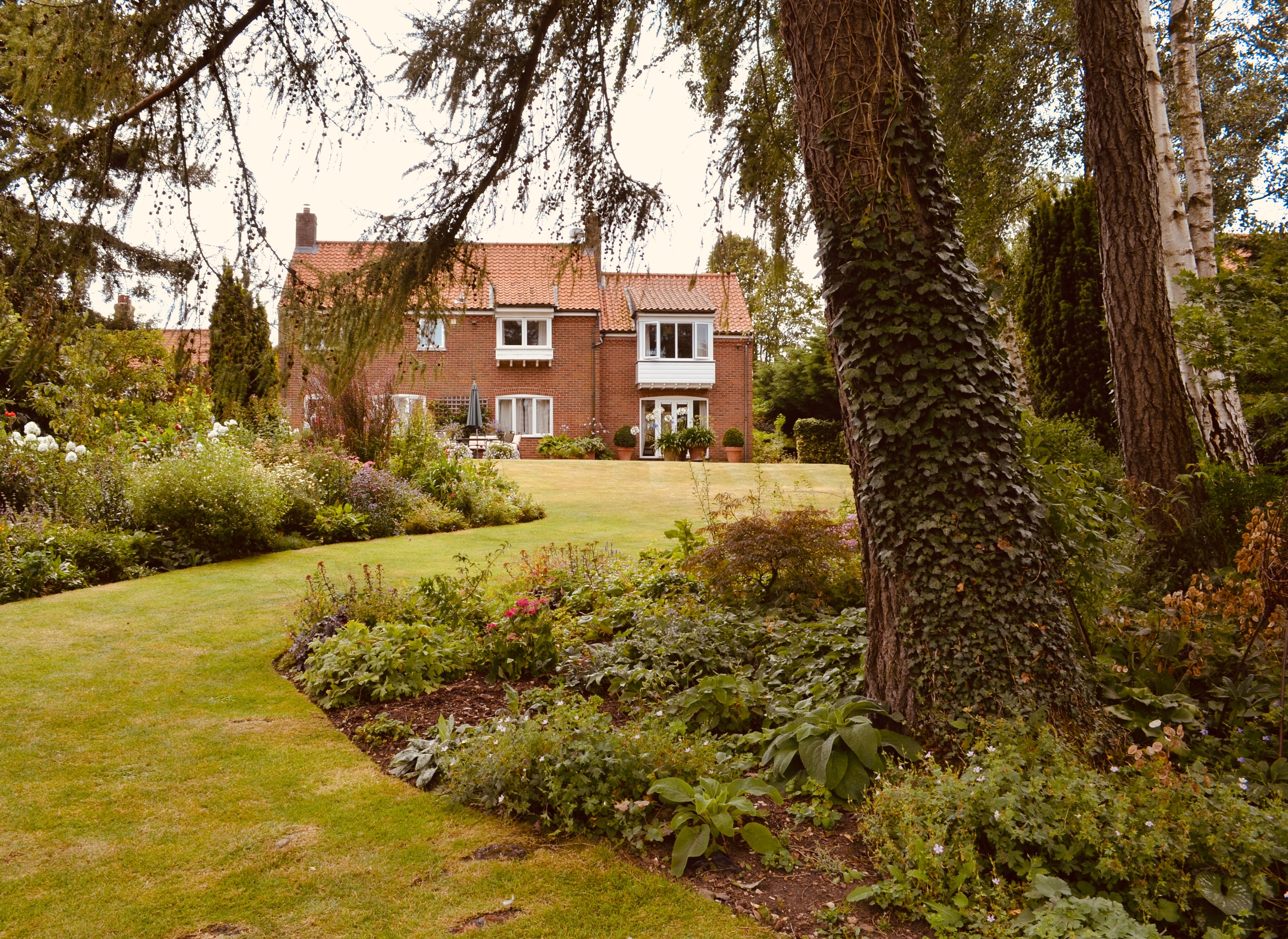 Brick house framed by a lush cottage garden and planted beds